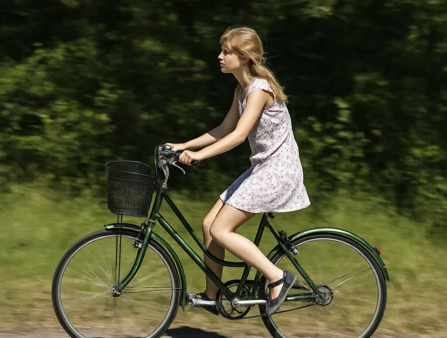 A girl riding a green bicycle past some trees